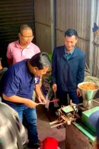 An artisan is instructing tourists on how to make an incense stick using a machine at the traditional incense-making village of Quang Phu Cau.