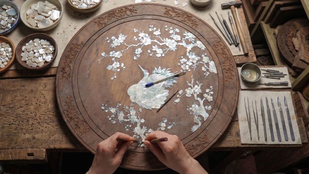 Mother-of-Pearl Inlay Village Tour: The artisan's hands are meticulously inlaying small pieces of mother-of-pearl onto the wooden base to create a work of art.